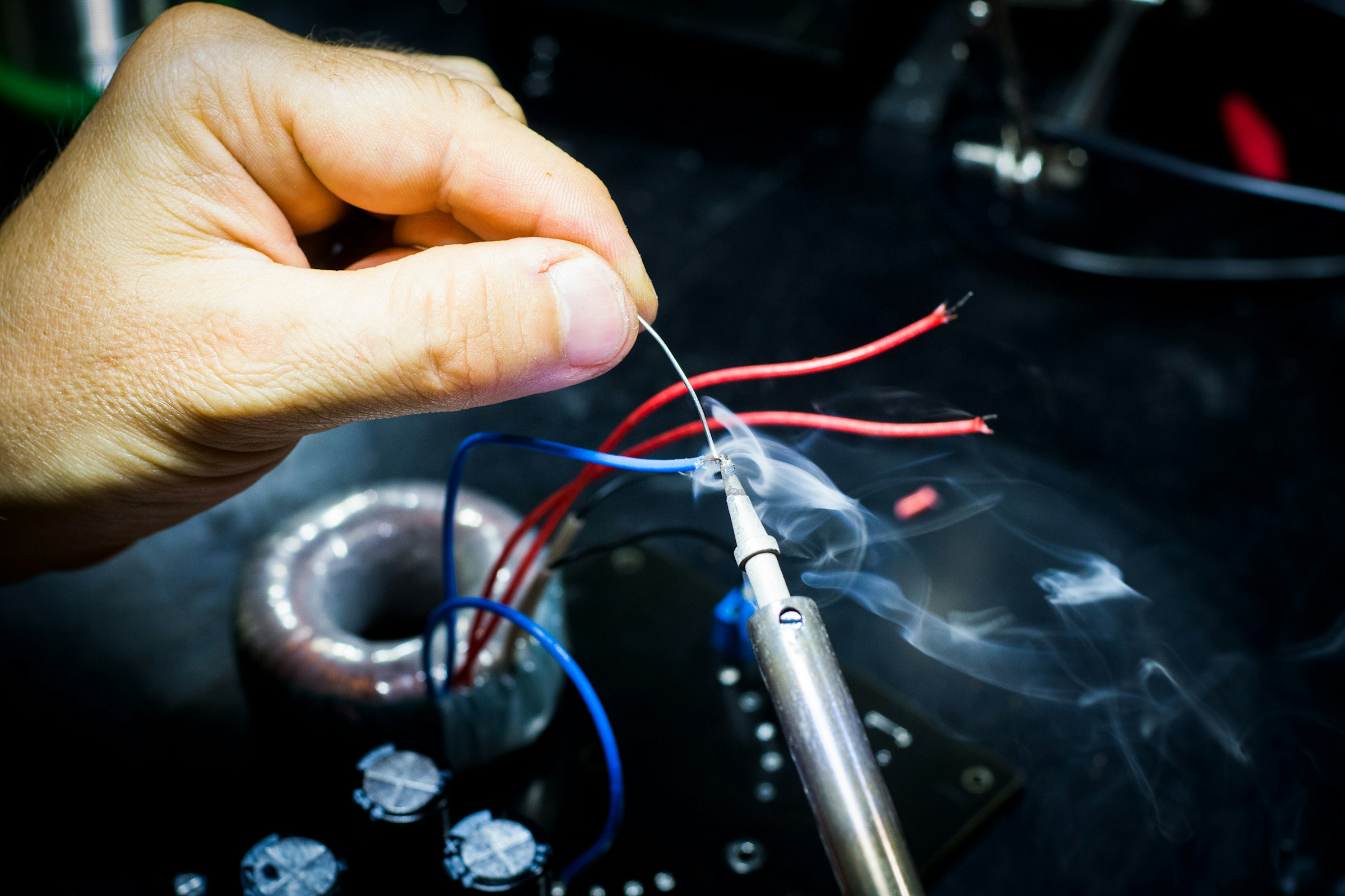 A hand soldering a wire joint on an electronics workbench, illustrating making an idea tangible